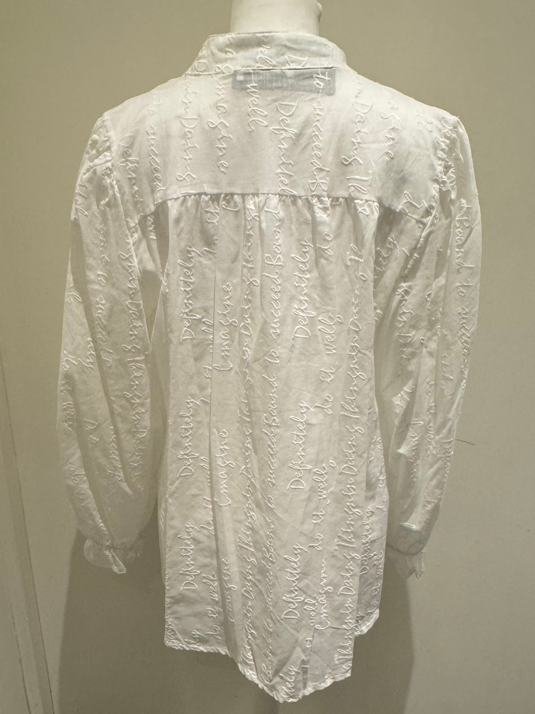 Deck by Decollage white embroidered cotton blouse featuring tonal script text, a split neckline, and ruffle cuffs. A breathable and elegant top ideal for smart-casual dressing.