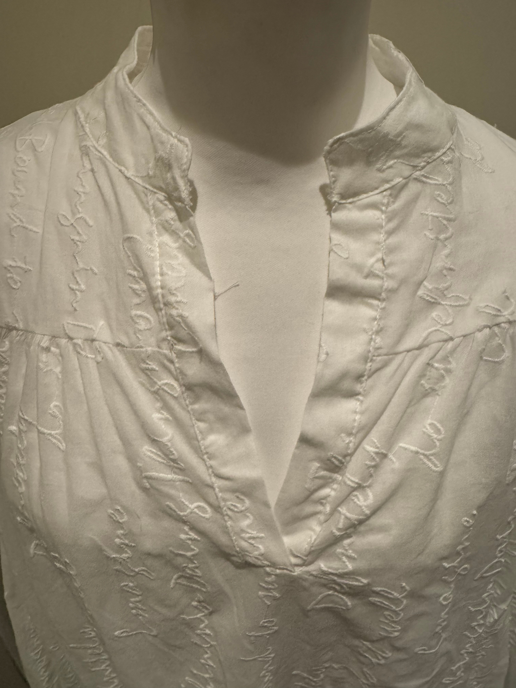 Deck by Decollage white embroidered cotton blouse featuring tonal script text, a split neckline, and ruffle cuffs. A breathable and elegant top ideal for smart-casual dressing.