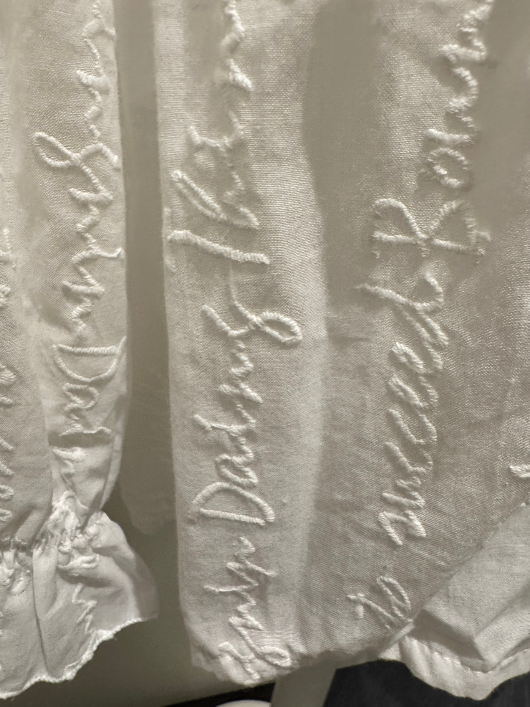 Deck by Decollage white embroidered cotton blouse featuring tonal script text, a split neckline, and ruffle cuffs. A breathable and elegant top ideal for smart-casual dressing.