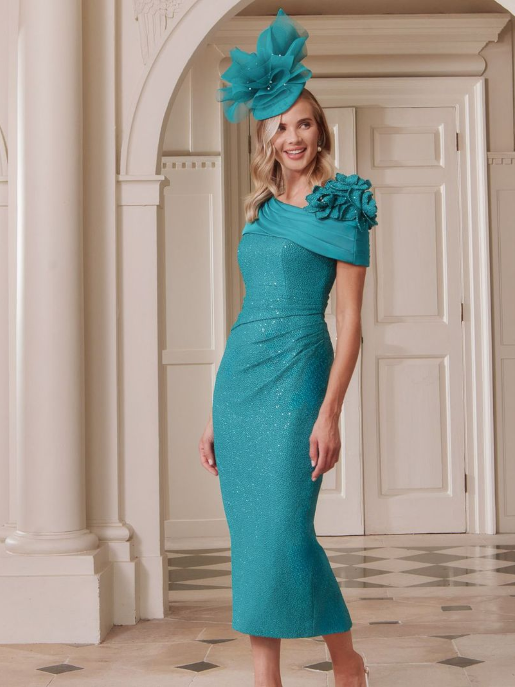 John Charles 29337A Peacock Dress with asymmetric bardot collar, sparkle stretch fabric, straight midi skirt and floral shoulder detailing.