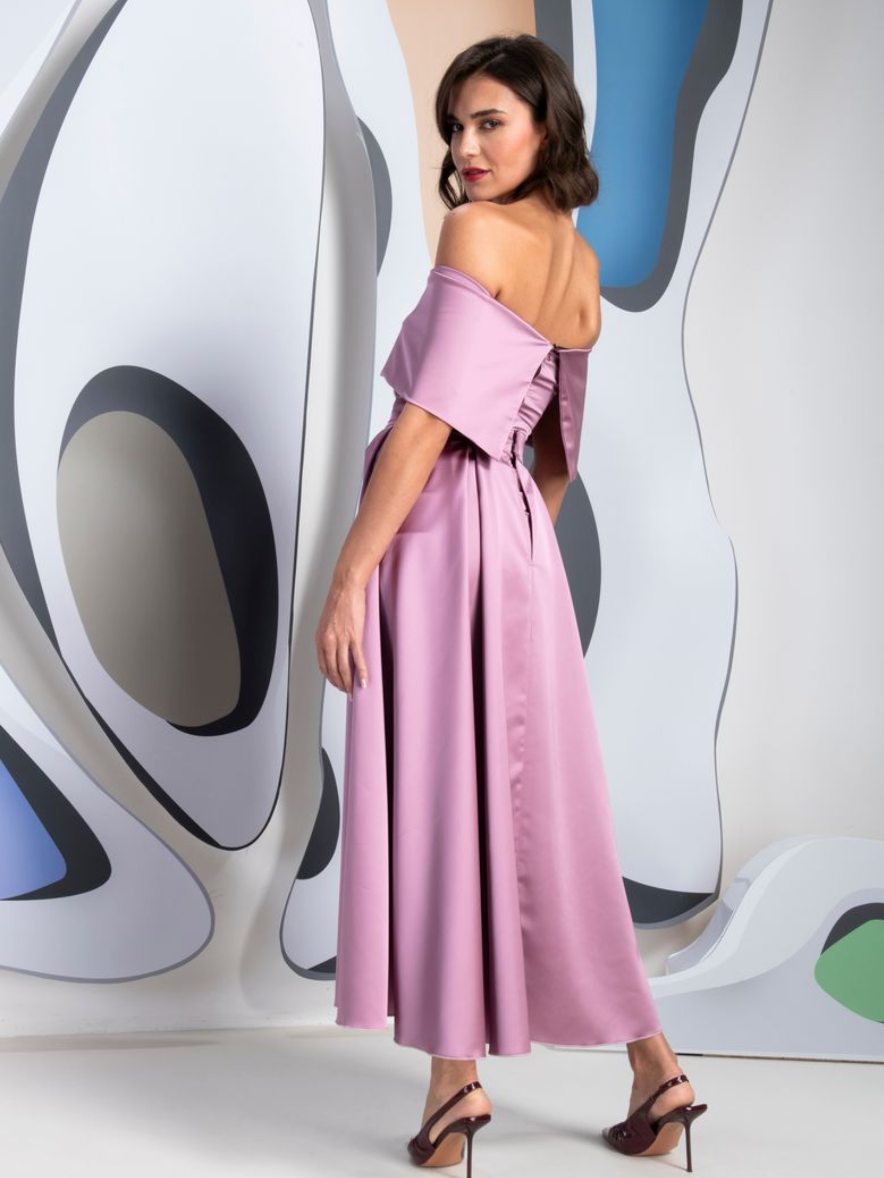 Kevan Jon Kris Lilac Dress with bardot neckline, ruched bodice, fitted skirt, flowing overskirt and oversized rosette detail.