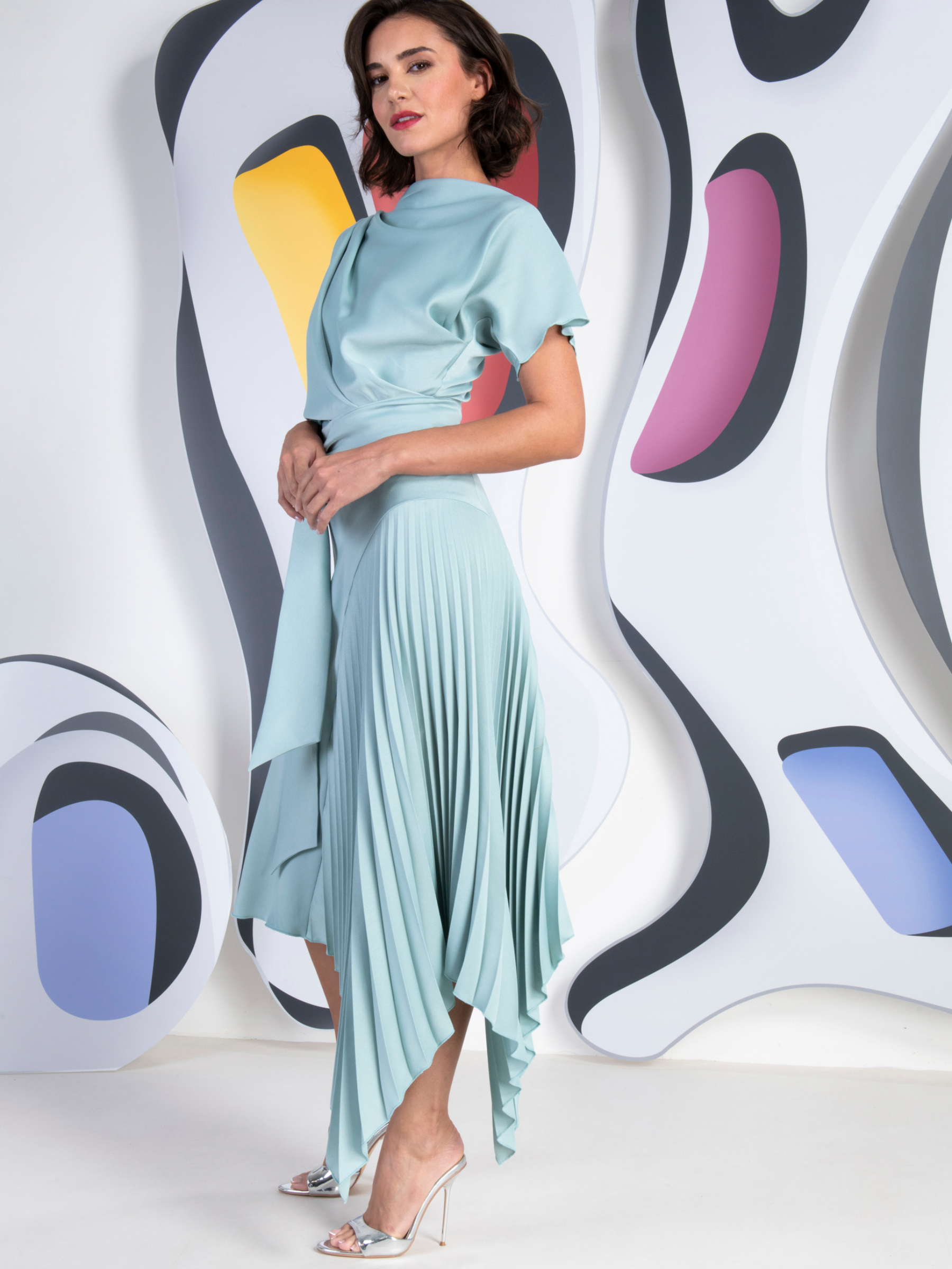 Kevan Jon Mila Pleat Dusty Blue Knee Dress in satin crepe with draped bodice, tie waist and asymmetric pleated skirt.