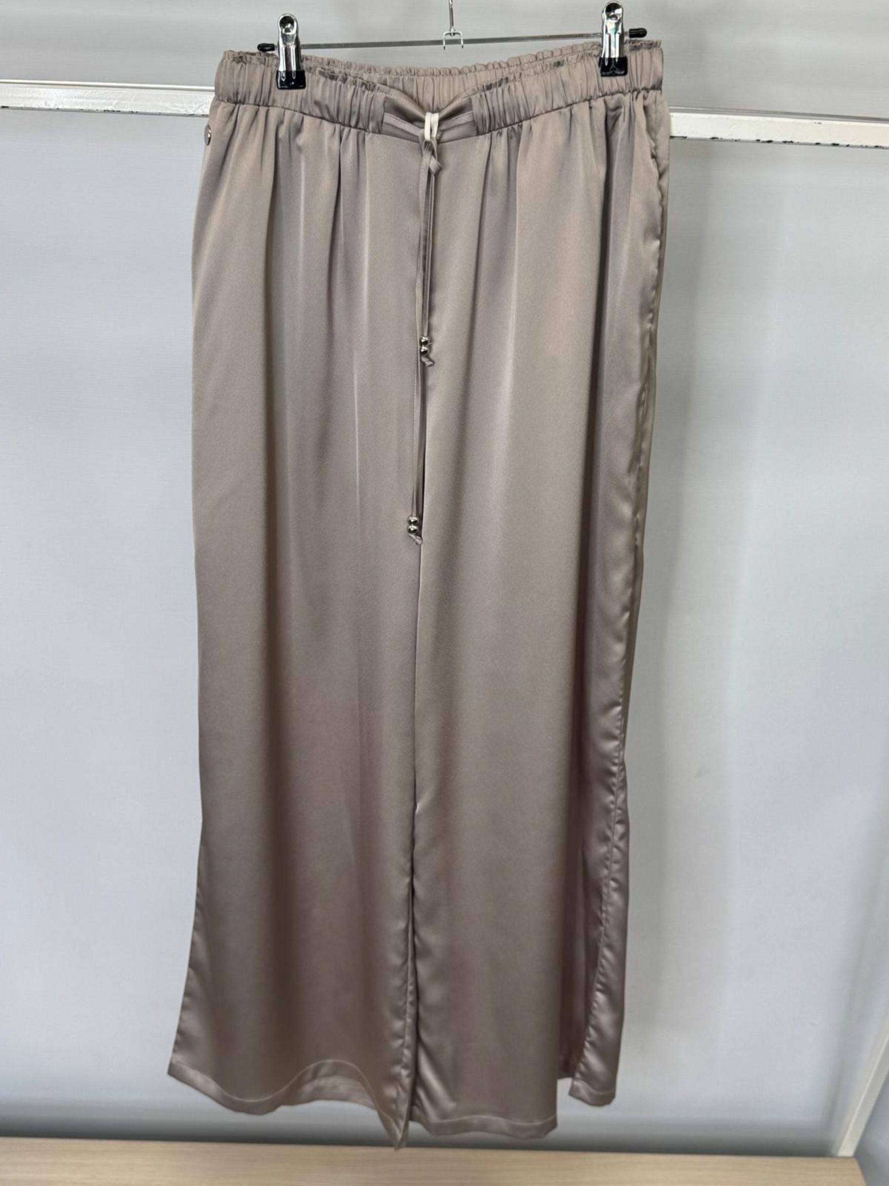 Brown satin trousers on a hanger against a white wall