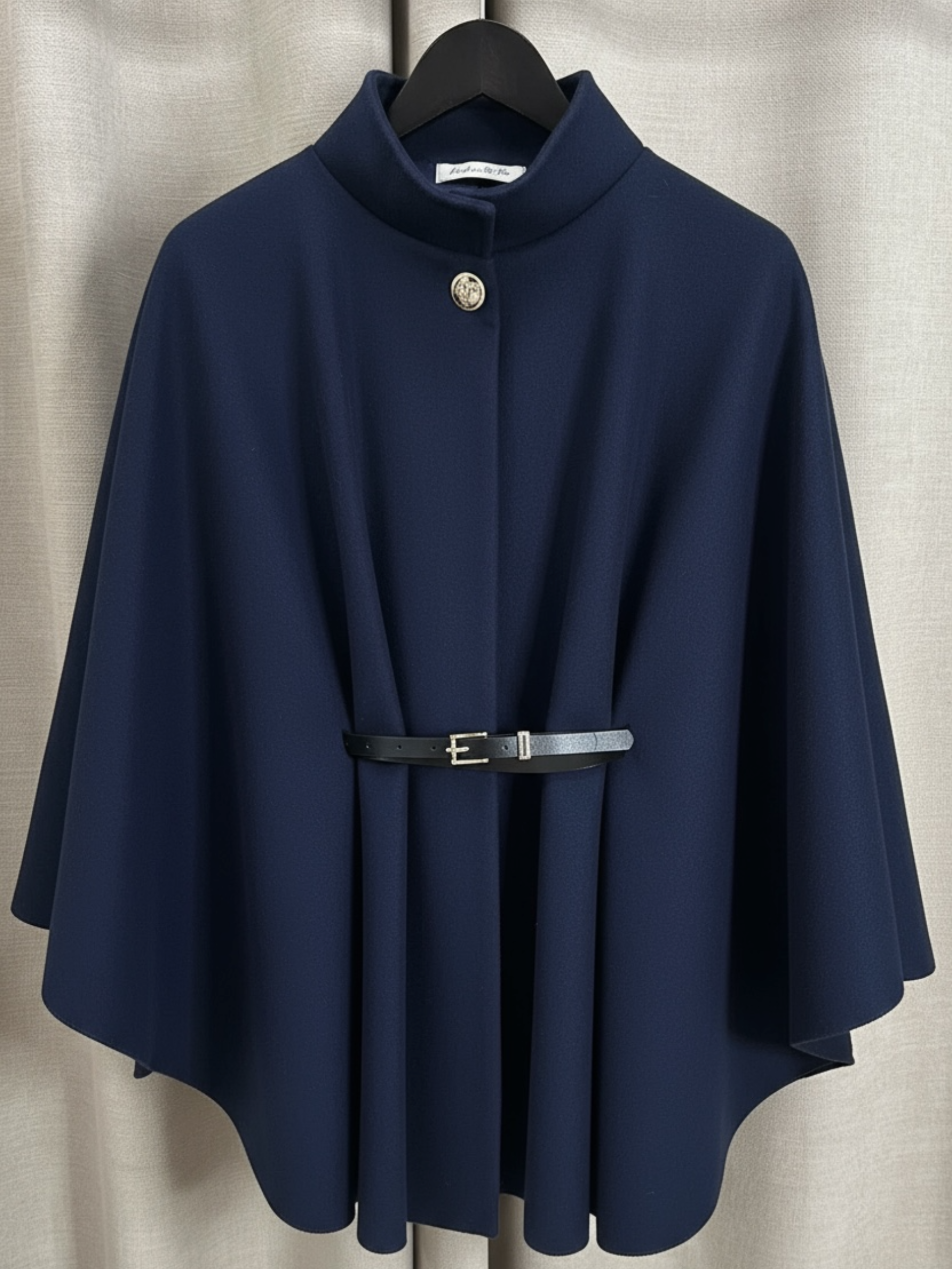 The QBAW25 RR Navy Carrie Cape features a structured silhouette with wide sleeves, a high neckline and elegant gold button detailing. Finished with a detachable belt for a flattering fit, this chic cape blends timeless tailoring with modern sophistication - perfect for layering over seasonal outfits.