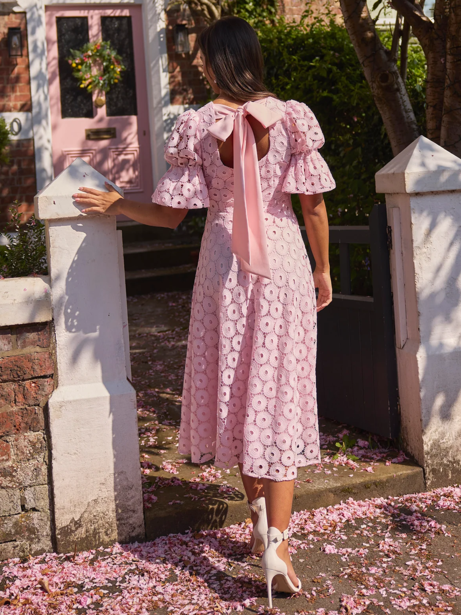 Pale pink skater midi dress with broderie-style fabric, puff sleeves and bow back detail.