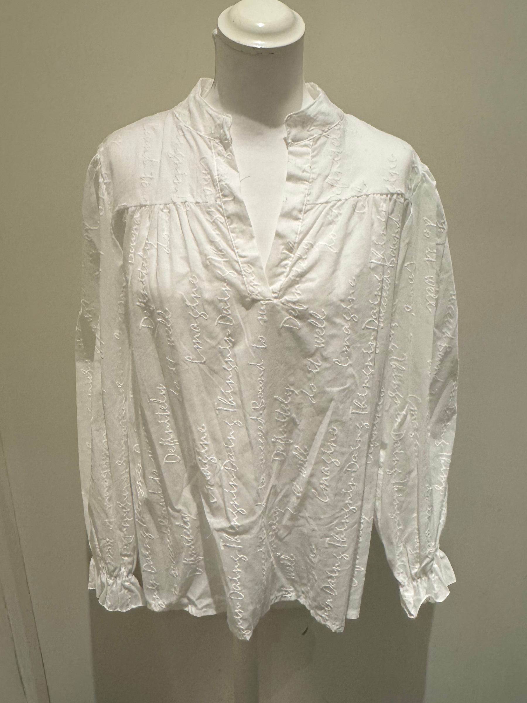 Deck by Decollage white embroidered cotton blouse featuring tonal script text, a split neckline, and ruffle cuffs. A breathable and elegant top ideal for smart-casual dressing.