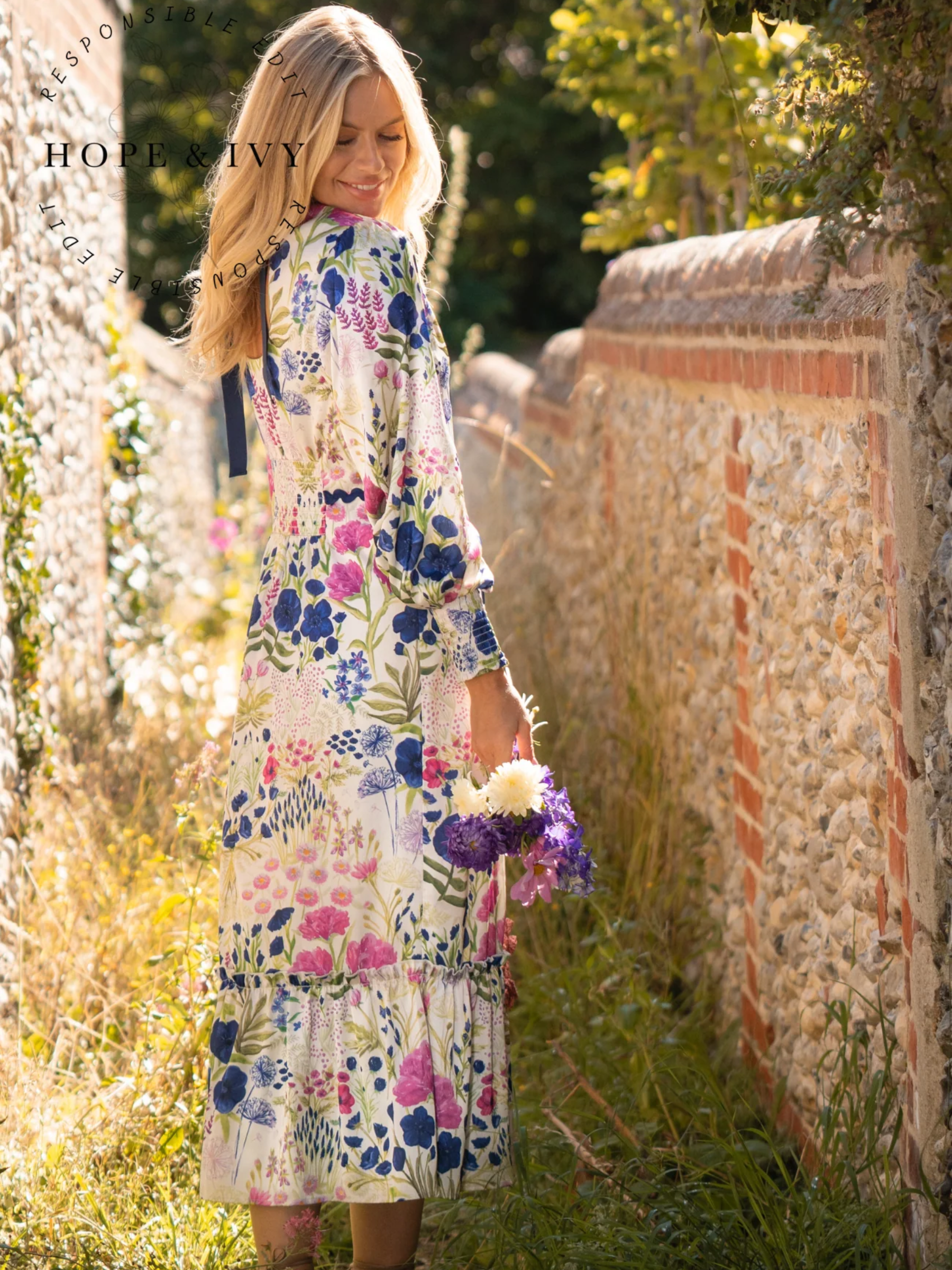 Hope & Ivy Caroline White Floral Maxi Dress – sustainable women’s satin floral print dress with blouson sleeves, frilled hem and tie-back detail. Ideal for weddings, garden parties and summer occasions.