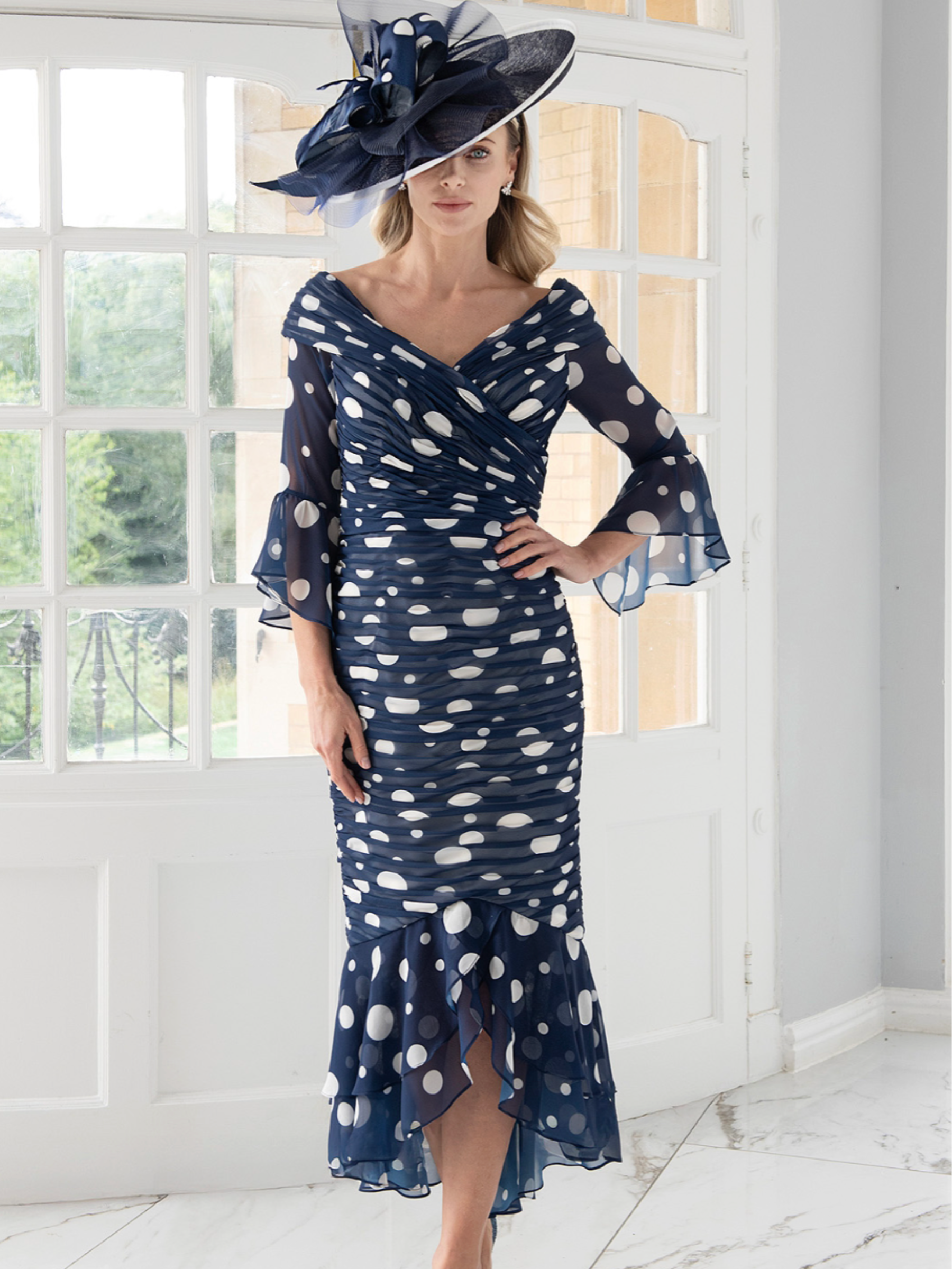 Irresistible IR8837TJ Navy/Ivory Dress with off-the-shoulder neckline, ruching throughout and a flowing fishtail hem — an elegant spot-print occasion dress perfect for weddings and special events.