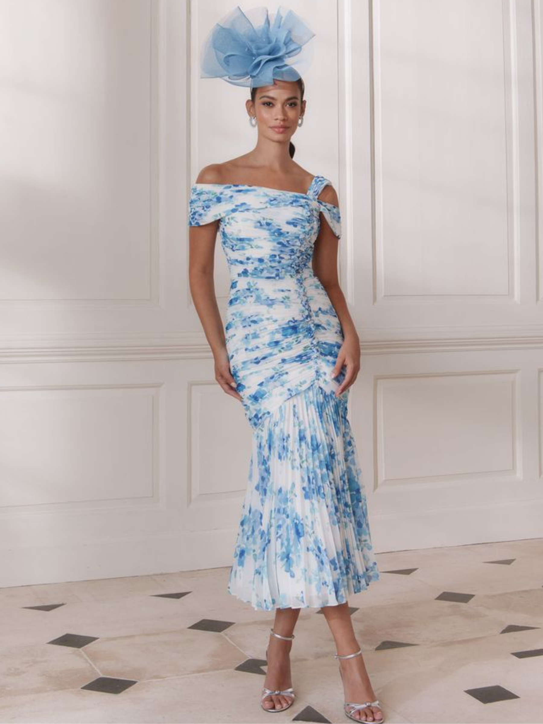 John Charles 66727A Blue Blossom Dress with off-the-shoulder wrap neckline, asymmetric strap detail, ruched bodice and pleated full-length chiffon skirt — a romantic floral occasion dress perfect for weddings and elegant events.