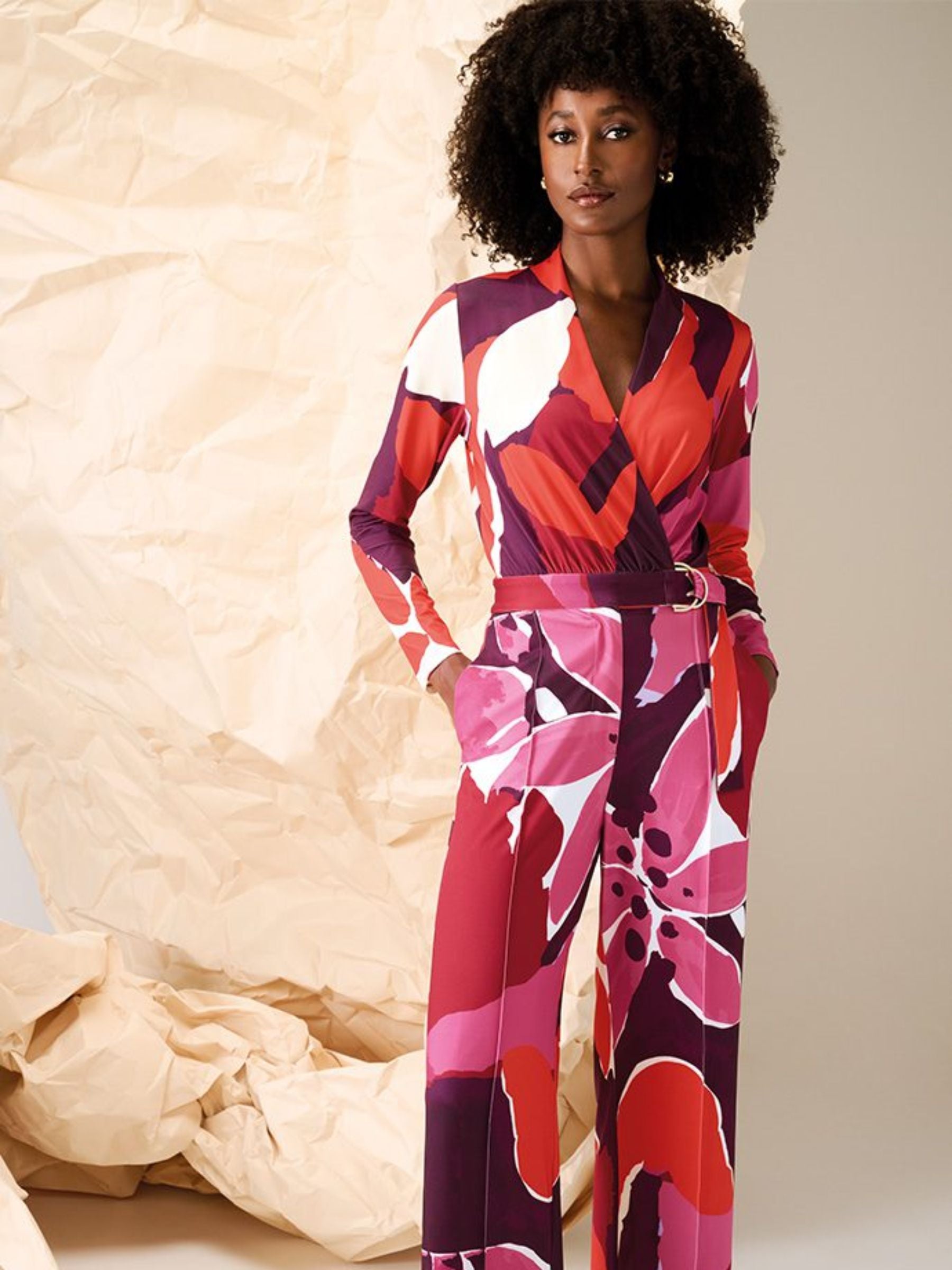 Full-length women’s printed jumpsuit by K Design featuring bold red, pink and purple abstract floral print, wrap-front neckline, long sleeves and belted waist - perfect for smart casual and evening wear styling.