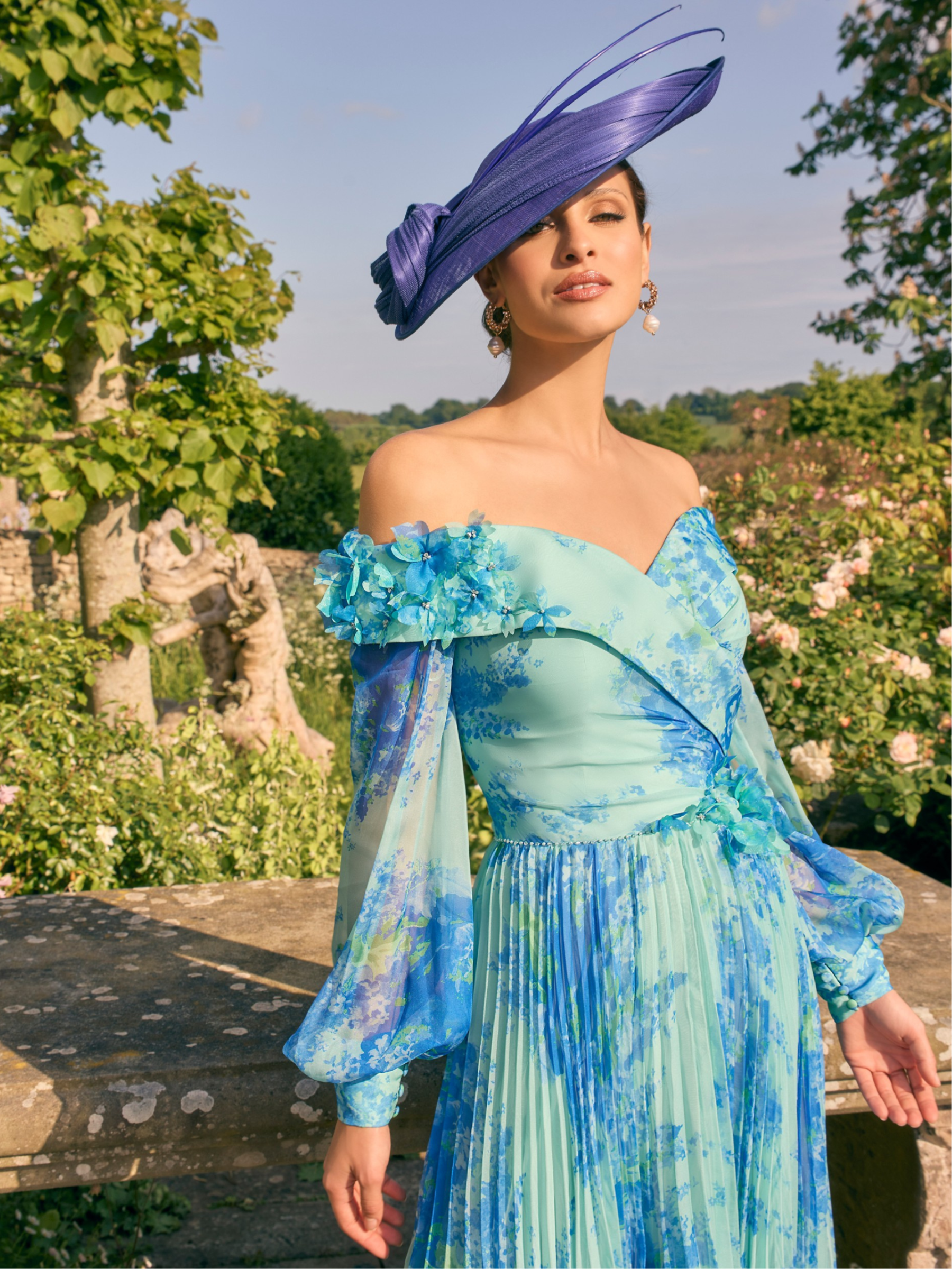 Veni Infantino 992780 Ocean Print Dress – off-the-shoulder chiffon print occasion dress with sheer bishop sleeves, pleated skirt and 3D floral appliqué waistband for weddings and race days.