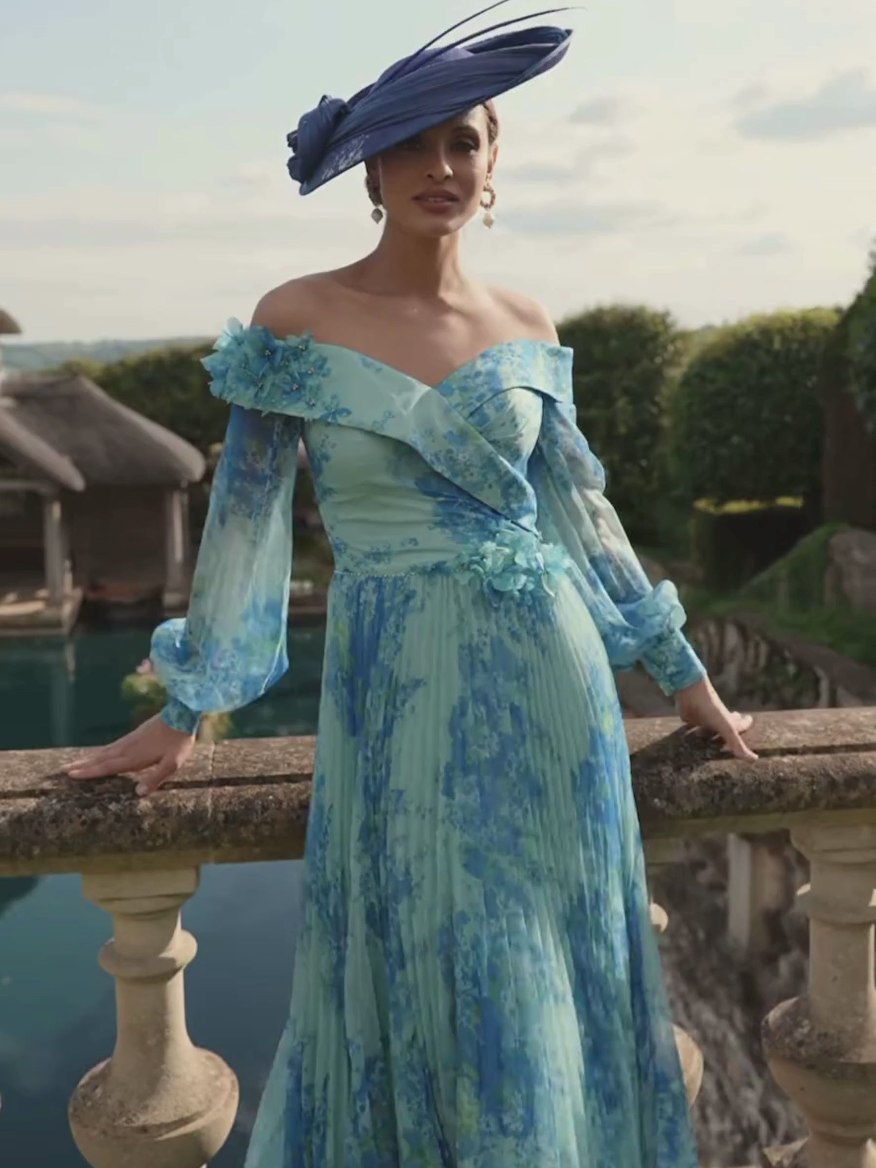 Veni Infantino 992780 Ocean Print Dress – off-the-shoulder chiffon print occasion dress with sheer bishop sleeves, pleated skirt and 3D floral appliqué waistband for weddings and race days.