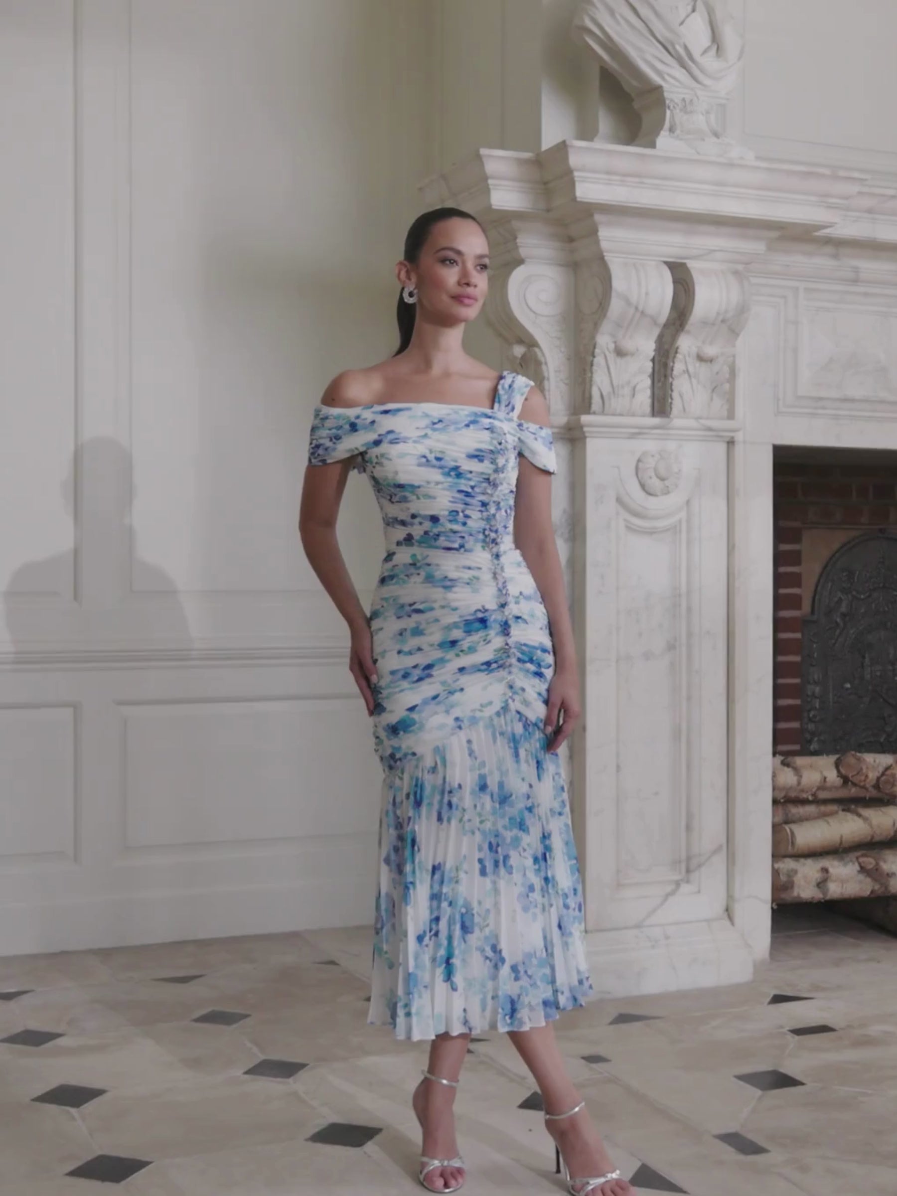 John Charles 66727A Blue Blossom Dress with off-the-shoulder wrap neckline, asymmetric strap detail, ruched bodice and pleated full-length chiffon skirt — a romantic floral occasion dress perfect for weddings and elegant events.